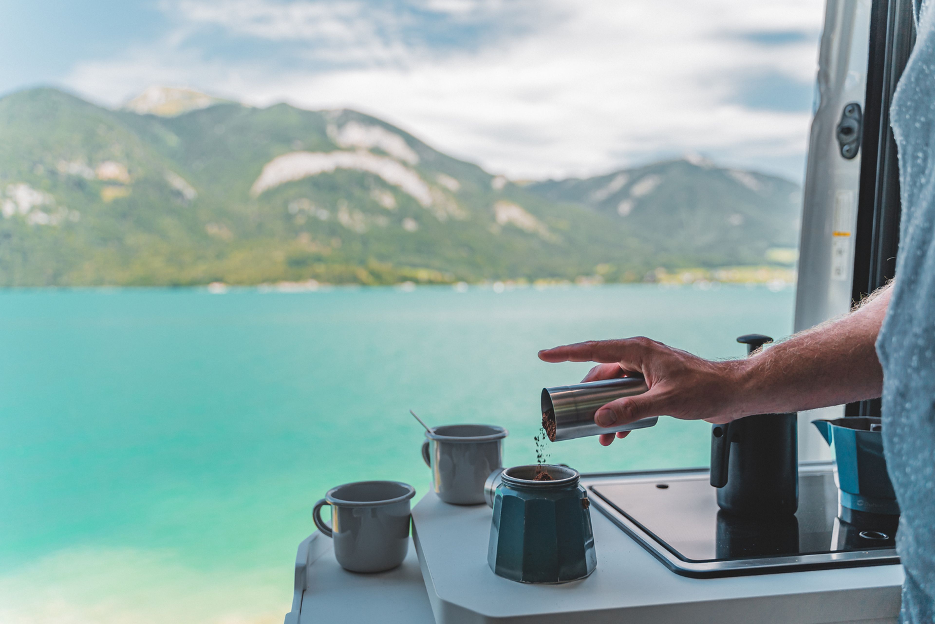 Kaffeekochen mit einer Moka-Kanne in einem Wohnmobil mit Blick auf einen See und eine schöne Bergkette