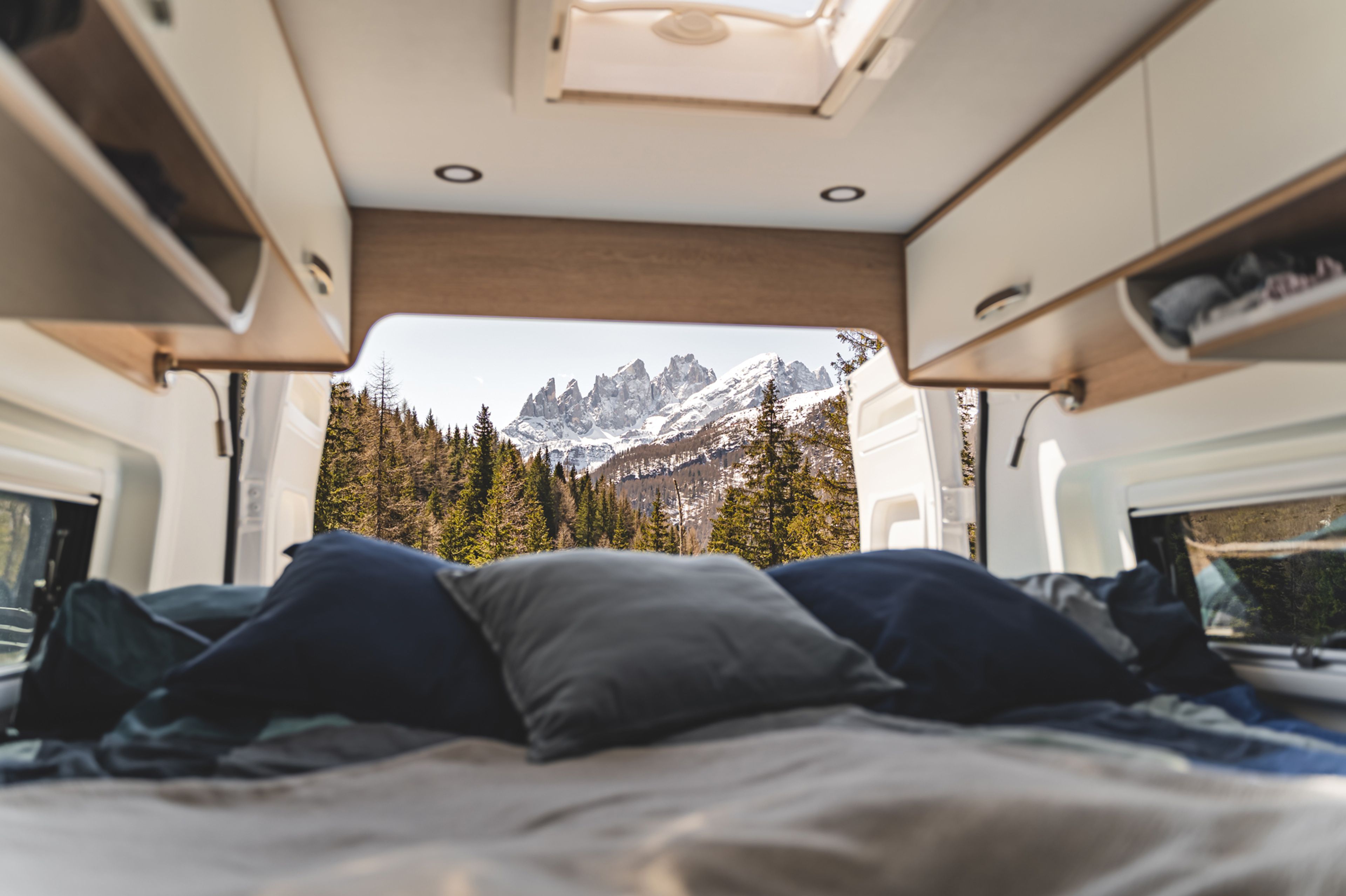 la vista di un accogliente letto caldo con cuscini all'interno di un camper che si affaccia su una catena montuosa innevata in Valle d'Aosta