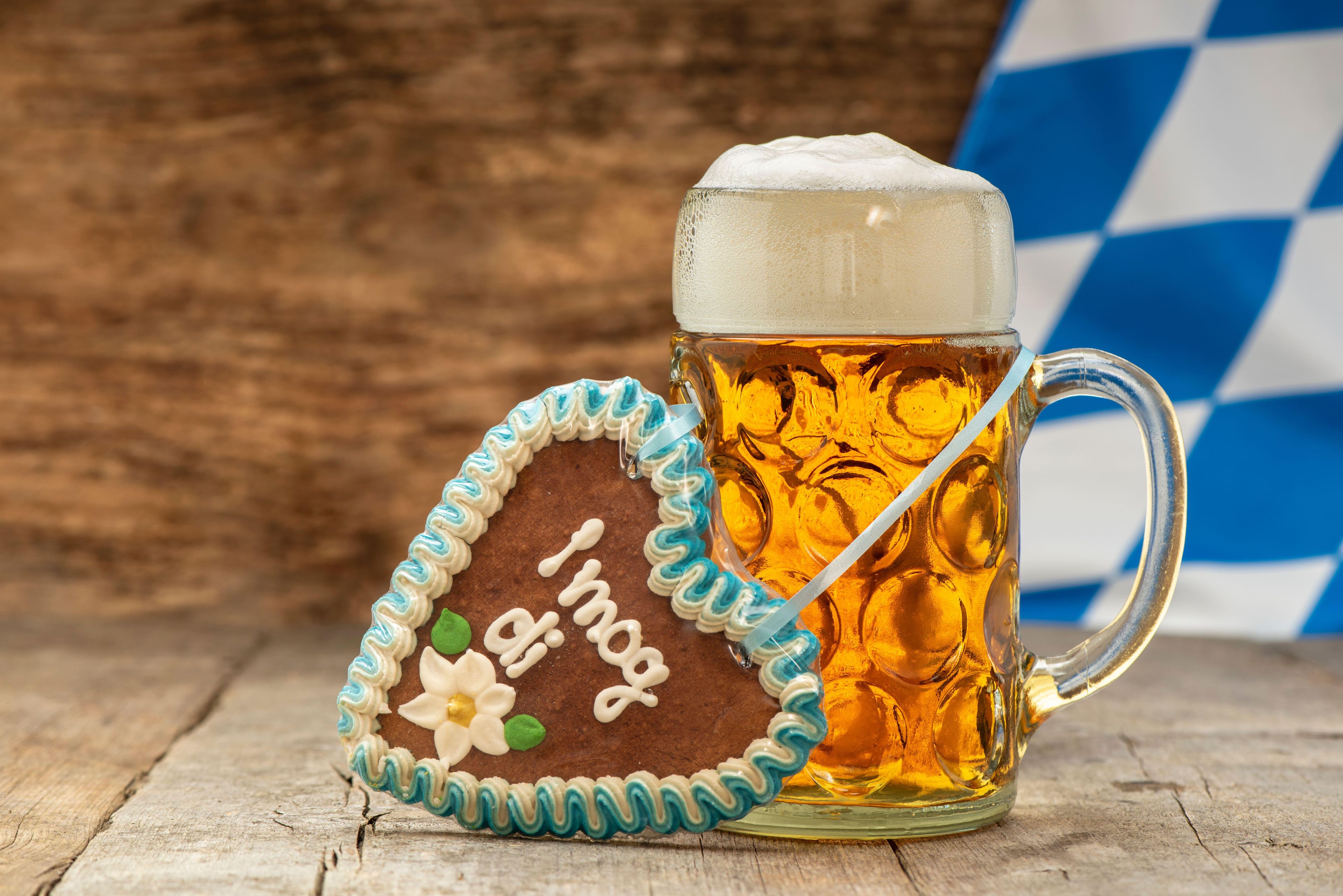 Maßkrug mit Bier hinter Lebkuchenherz vor bayrischer Flagge auf Holzboden