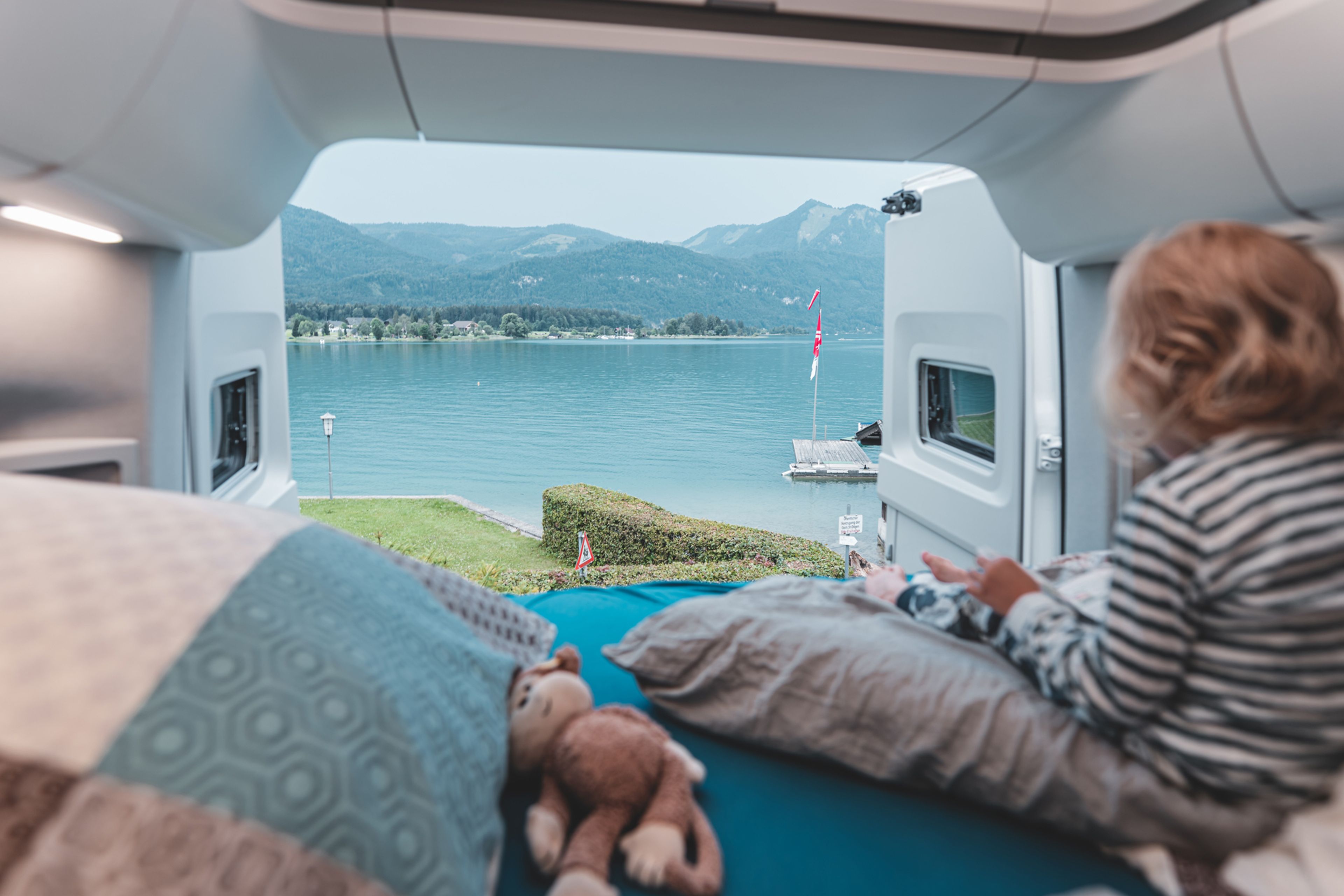 un bambino che legge dall'interno del letto del camper VW Grand California con vista sul Lago Maggiore