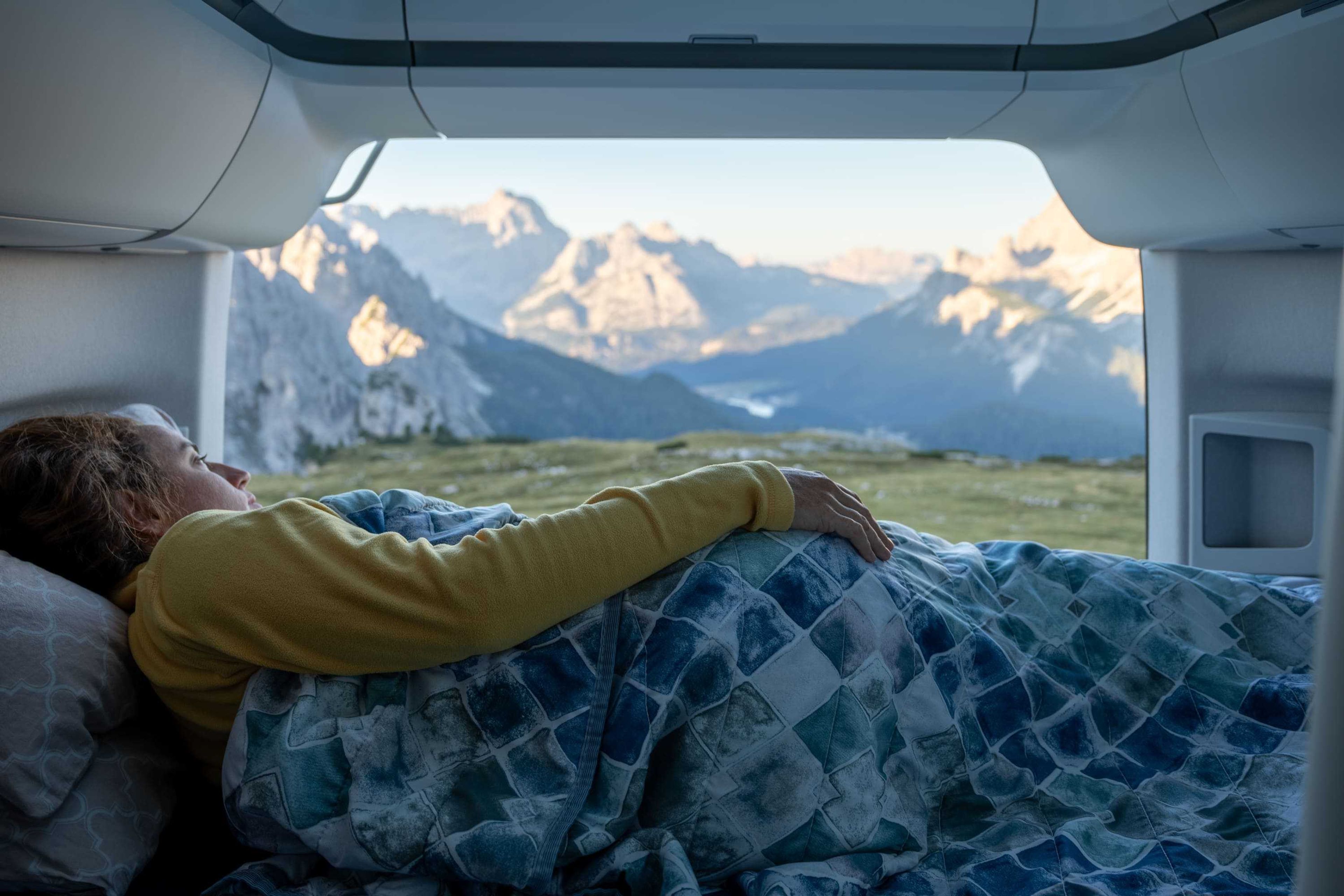 ragazza guarda la natura e le montagne sullo sfondo dal suo letto nel camper