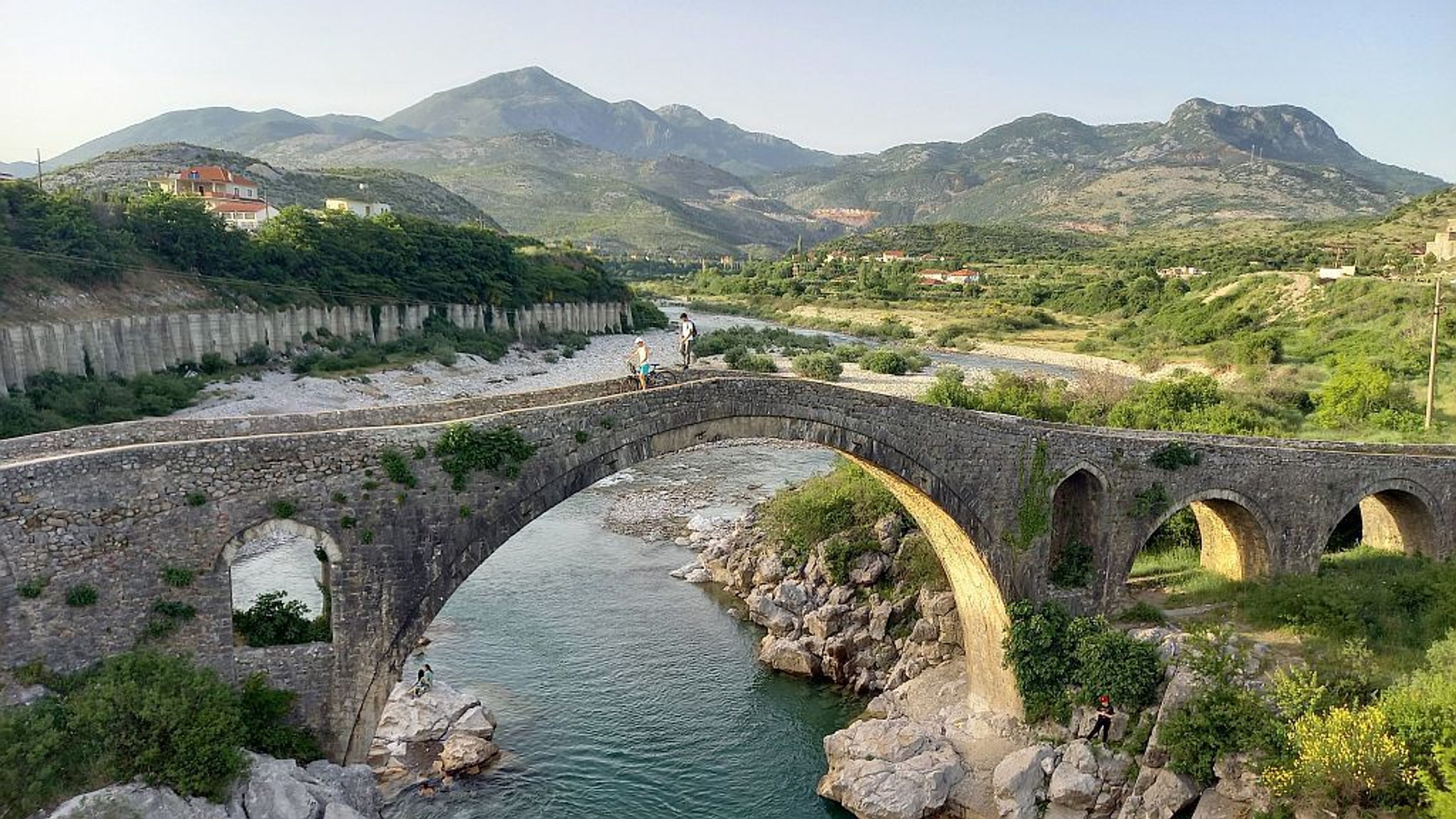 Paesaggio con due ragazzi su un ponte antico e montagne sullo sfondo in Albania