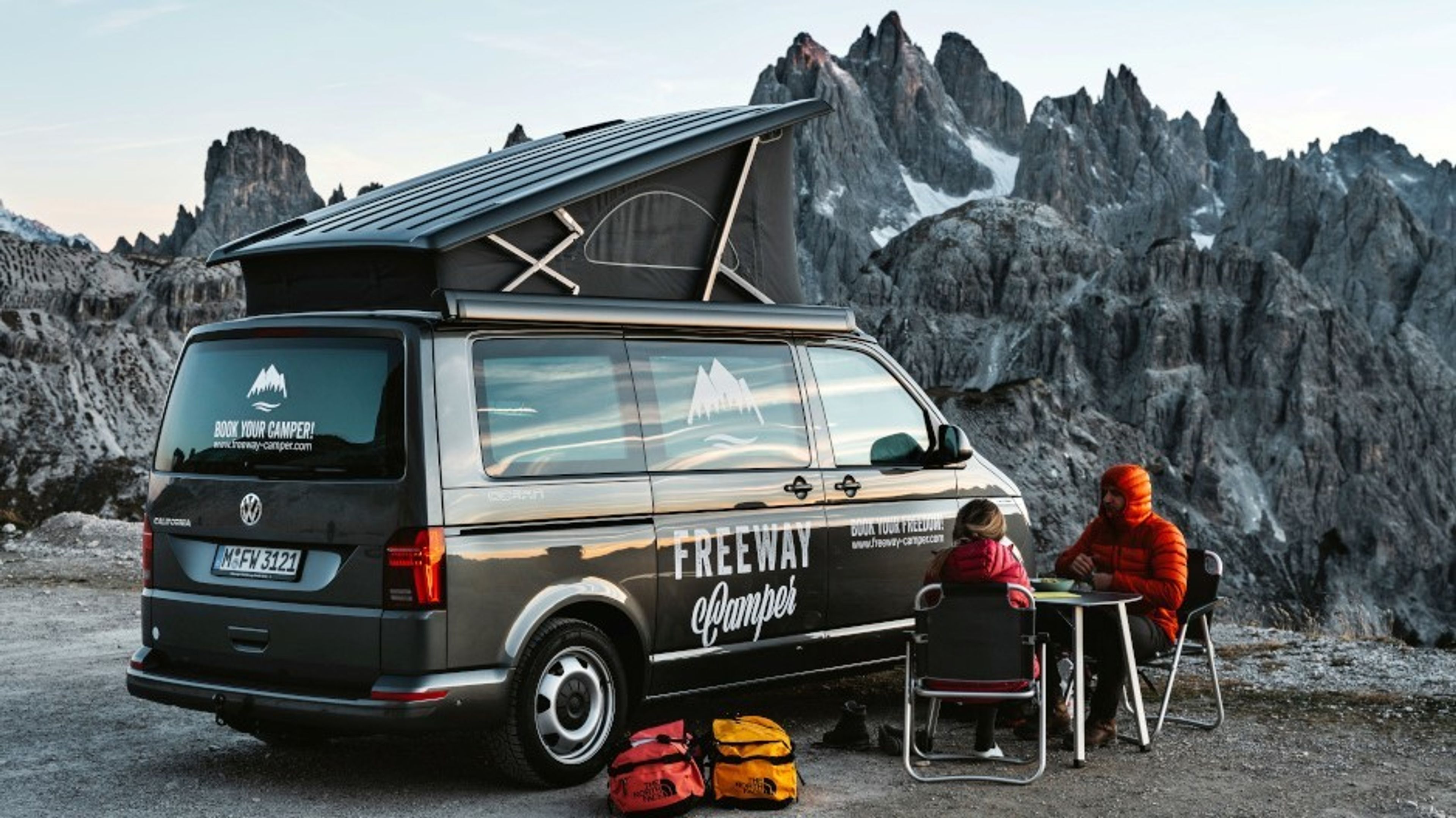 Two people sitting in front of a VW van in the wintry mountains