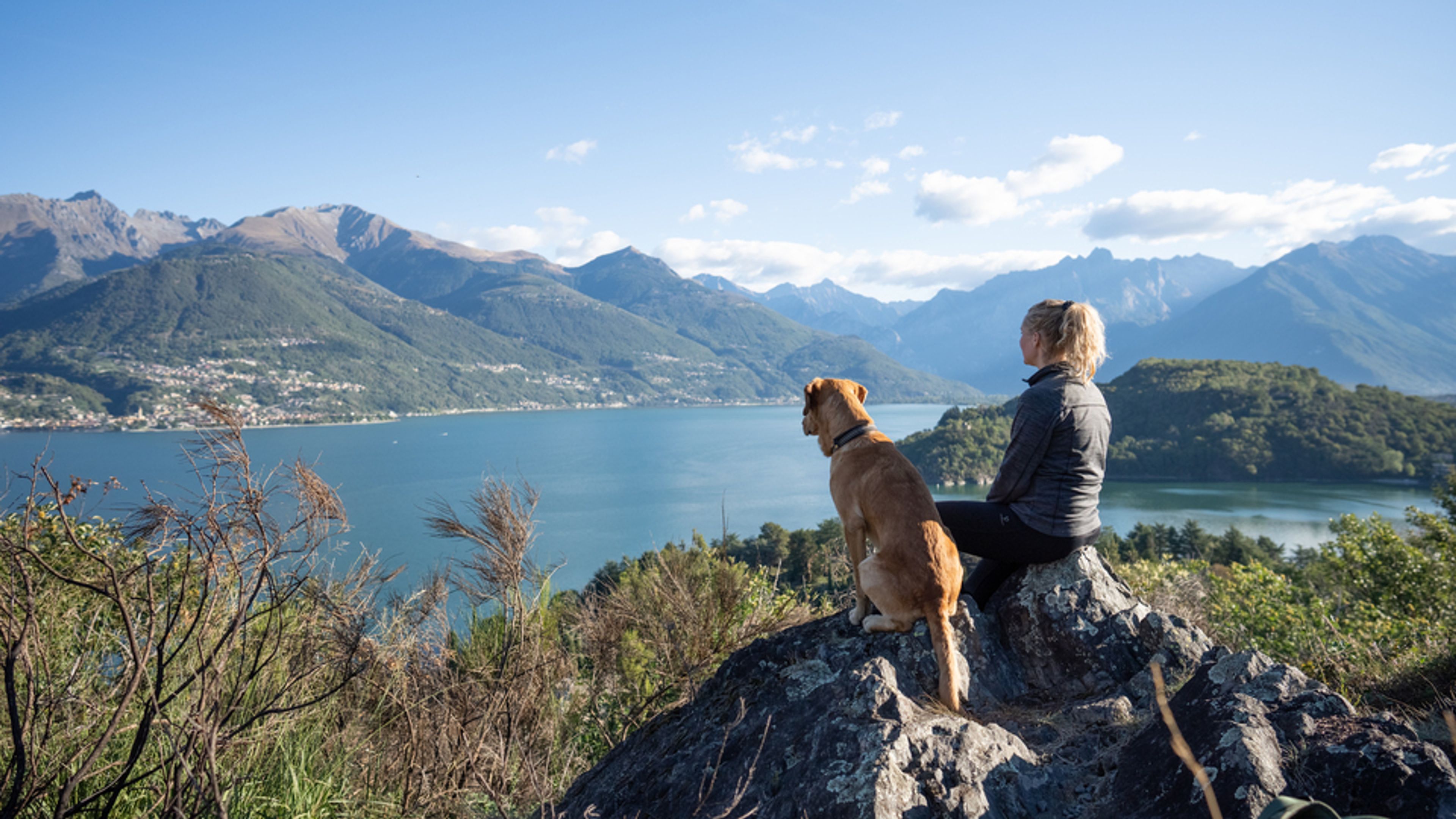 A woman and her dog on top of a mountain overlooking the breathtaking view of Lake Como, Italy