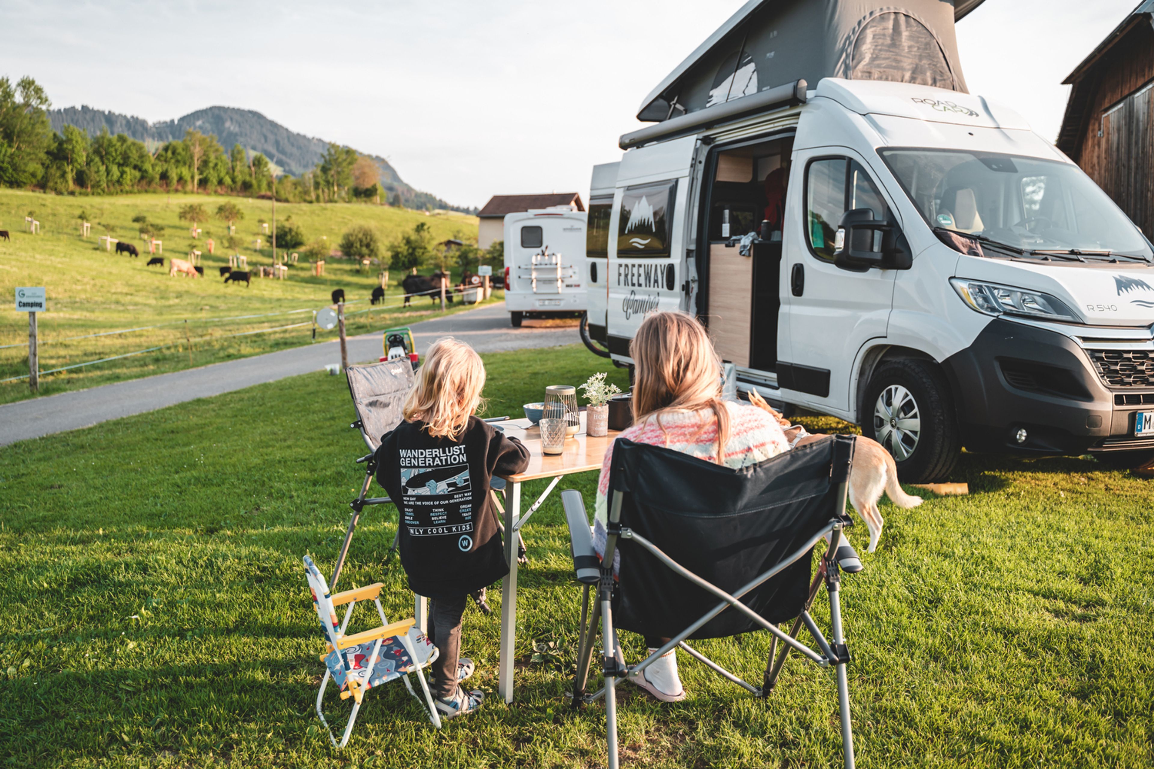 Viaggi in camper economici: VW Bulli T6.1 California Ocean nel verde delle montagne con bambini e un cane in Svizzera