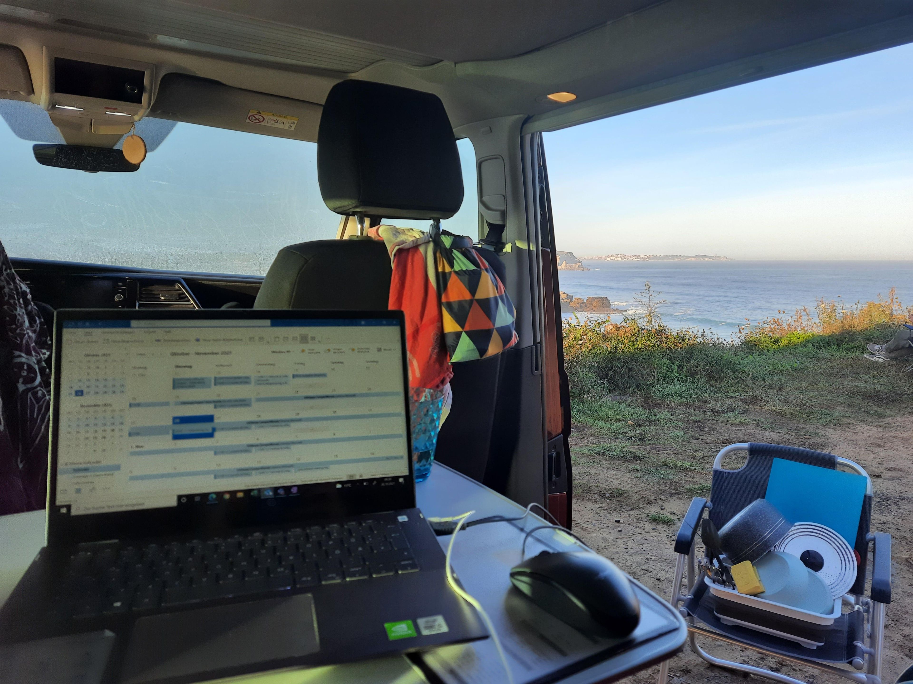 Laptop in the camper with a view of the sea and a cliff.