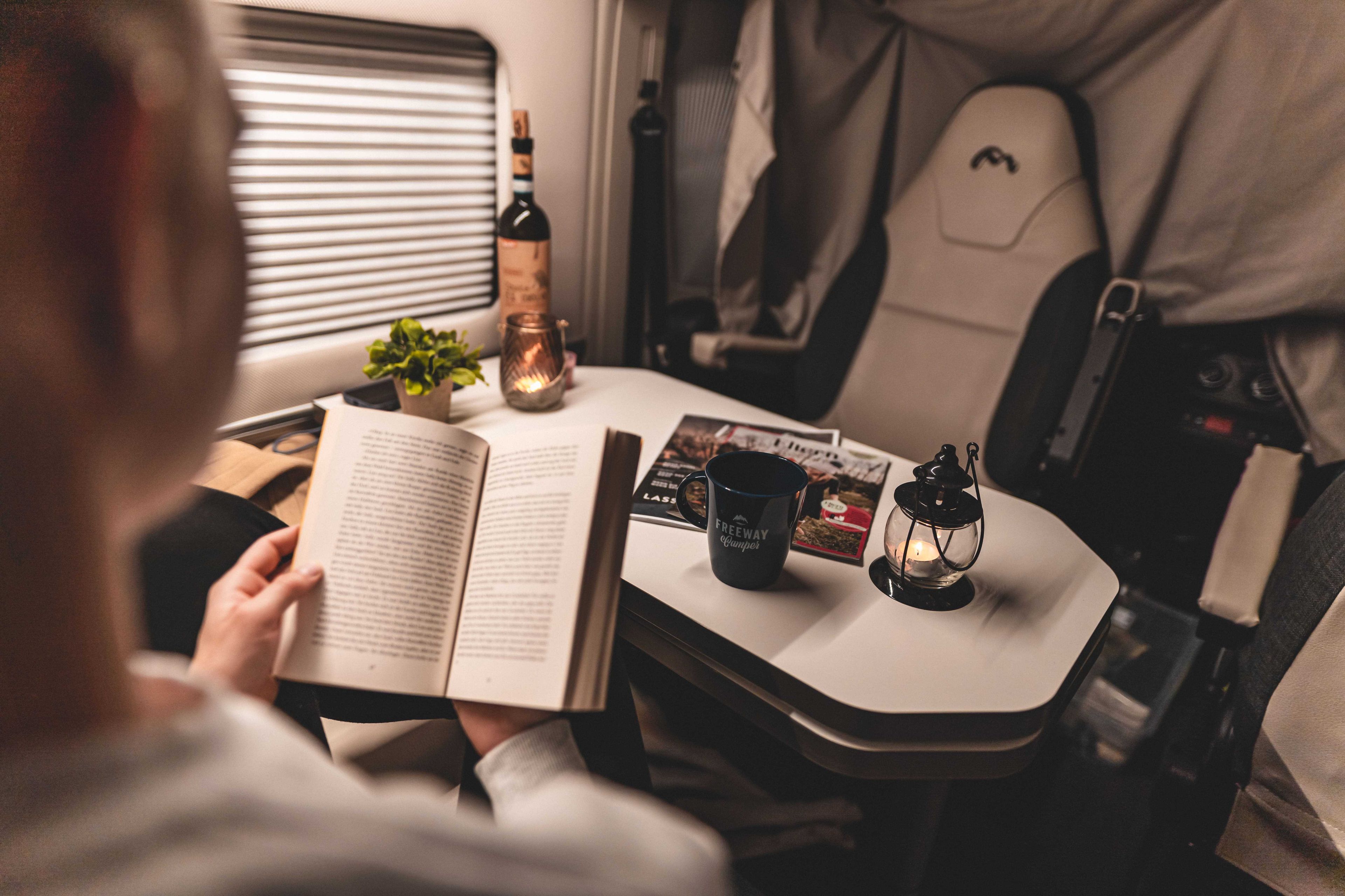 Persona che legge un libro con un bicchiere di vino in un'area salotto di un camper