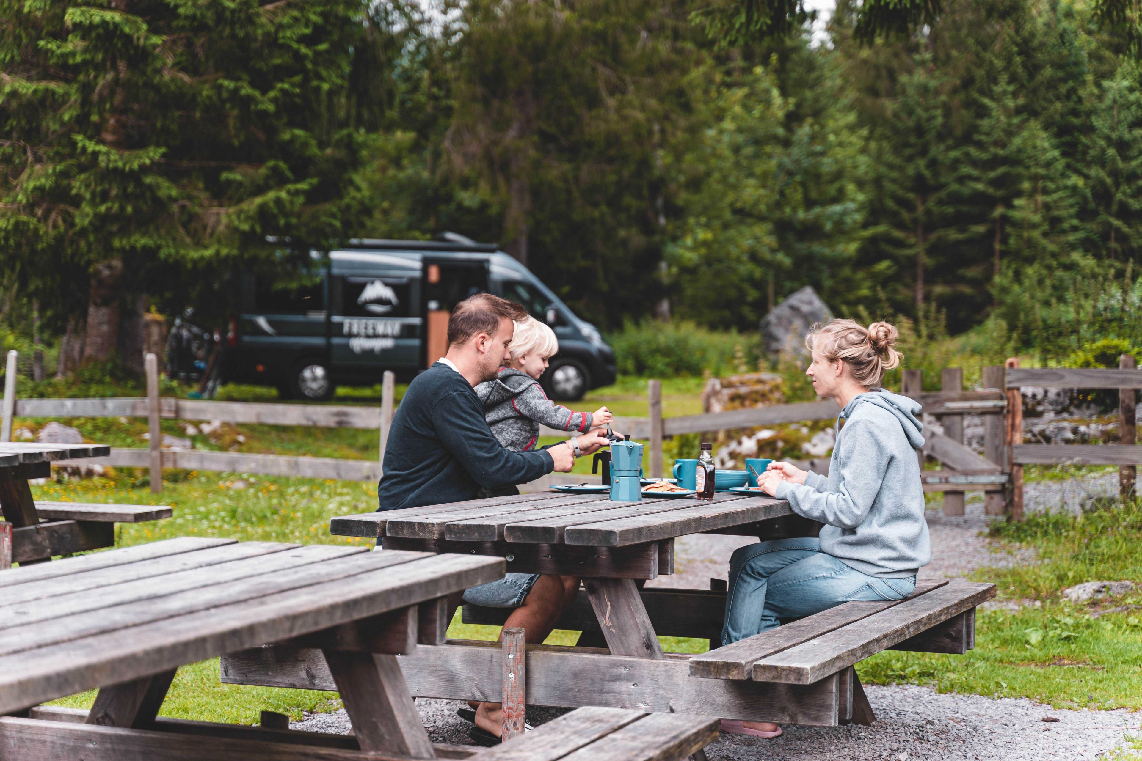 Famiglia con bambino seduto a un tavolo da picnic nella natura davanti a un camper verde