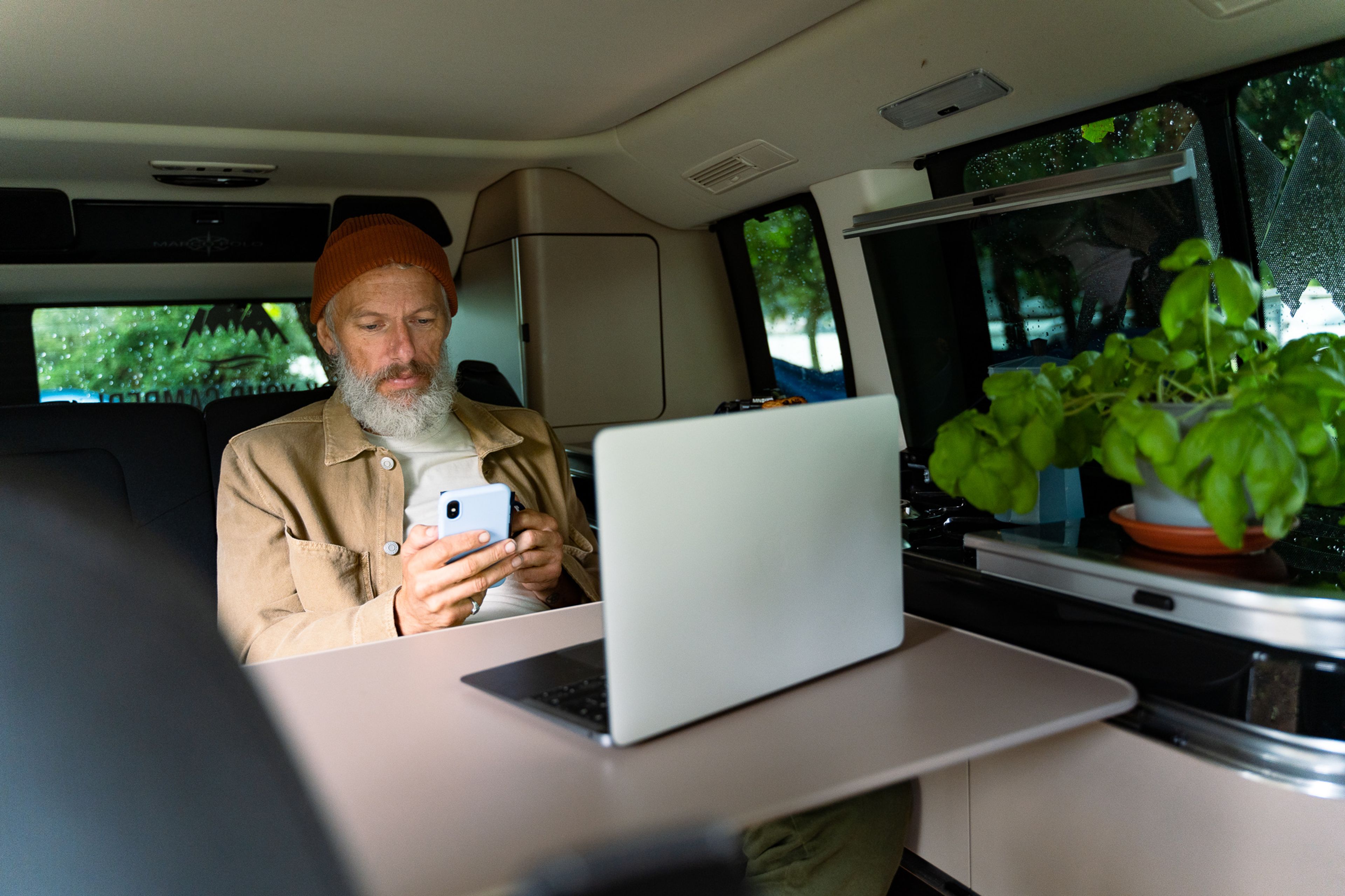 Un uomo usa il suo telefono e il suo computer portatile in un camper per lavorare a distanza