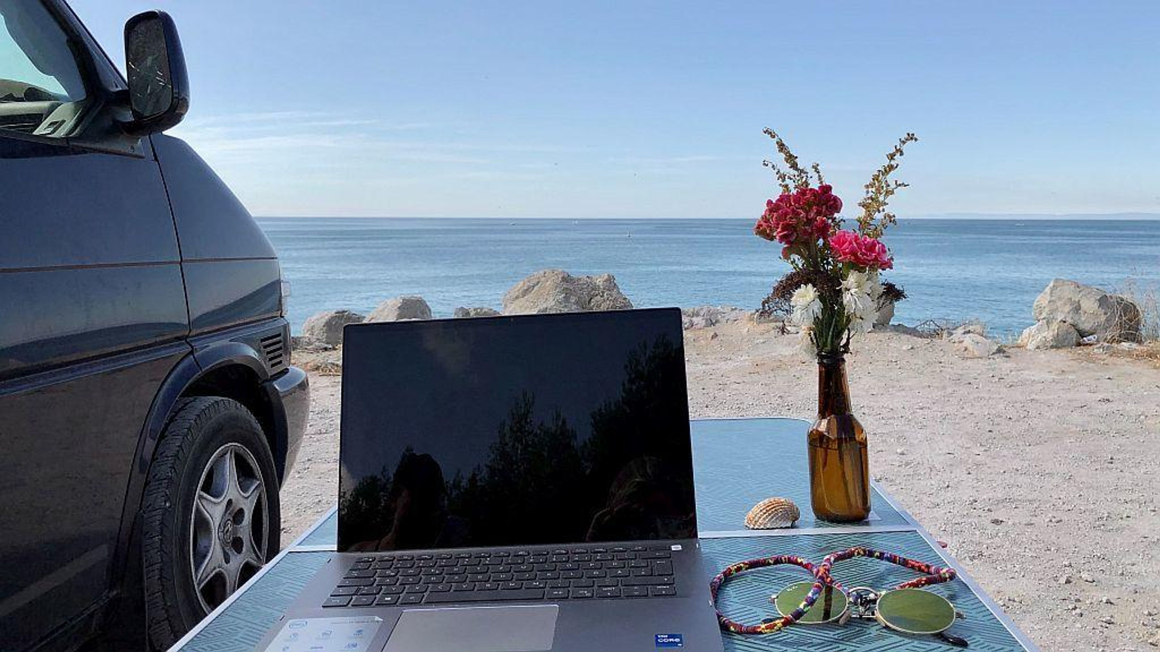 Tavolino con laptop fronte mare sulla spiaggia di sabbia del Portogallo e camper van