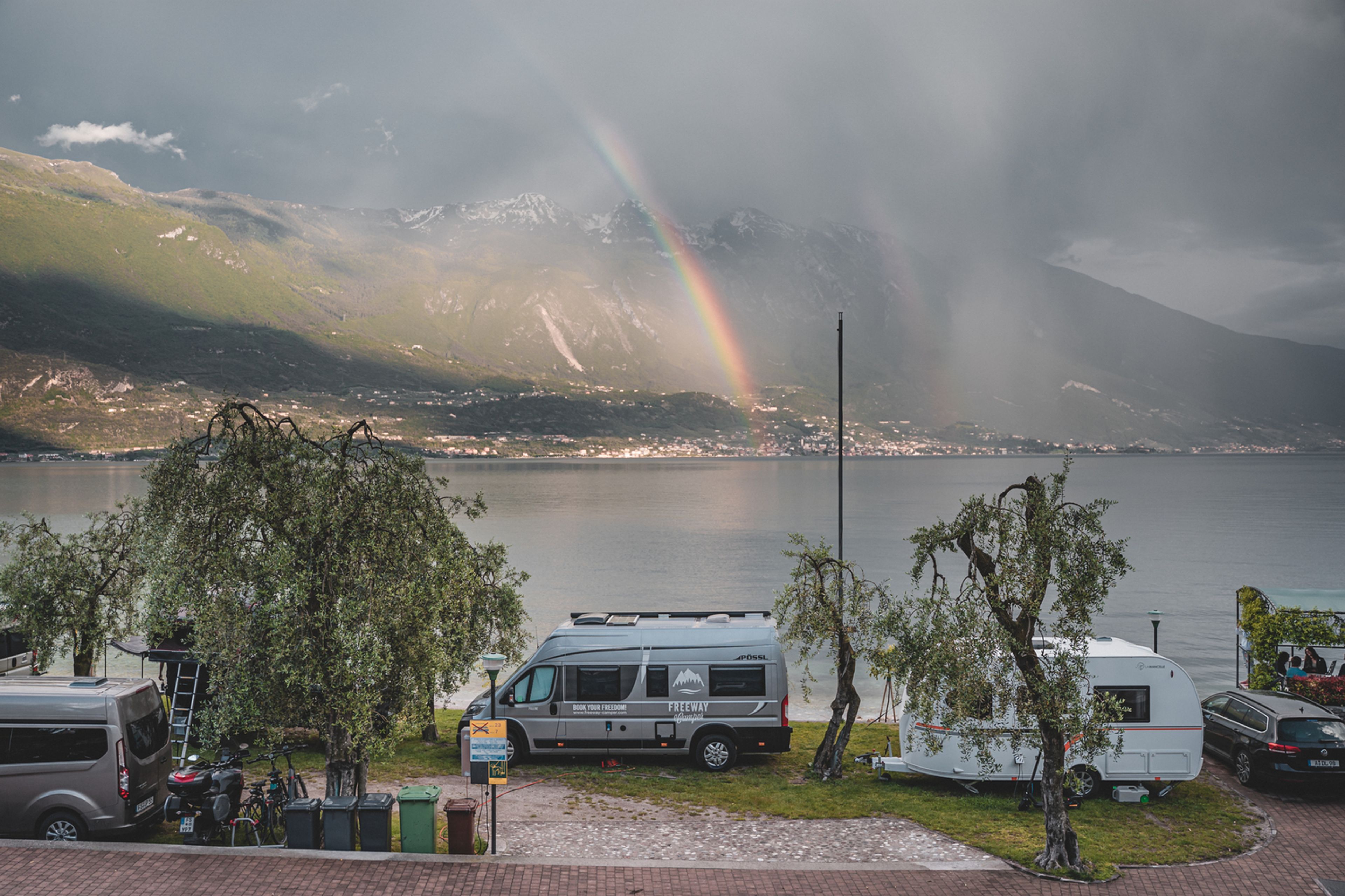 Camper in un campeggio direttamente sul lago di Garda. Sullo sfondo si vede un arcobaleno.