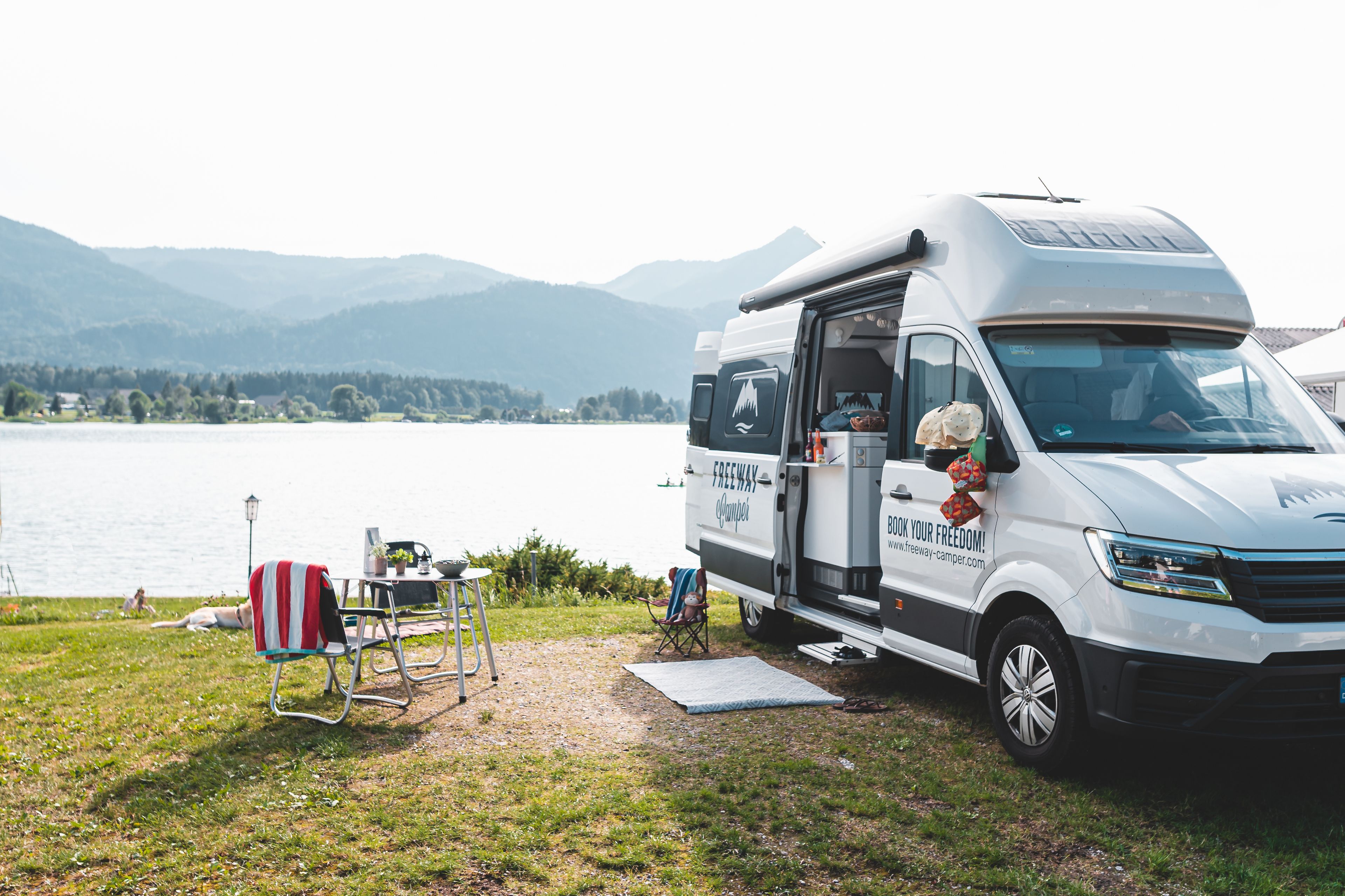 un parcheggio per camper VW Grand California sul Lago Maggiore con sedie e tavolo per tutta la famiglia con i bambini