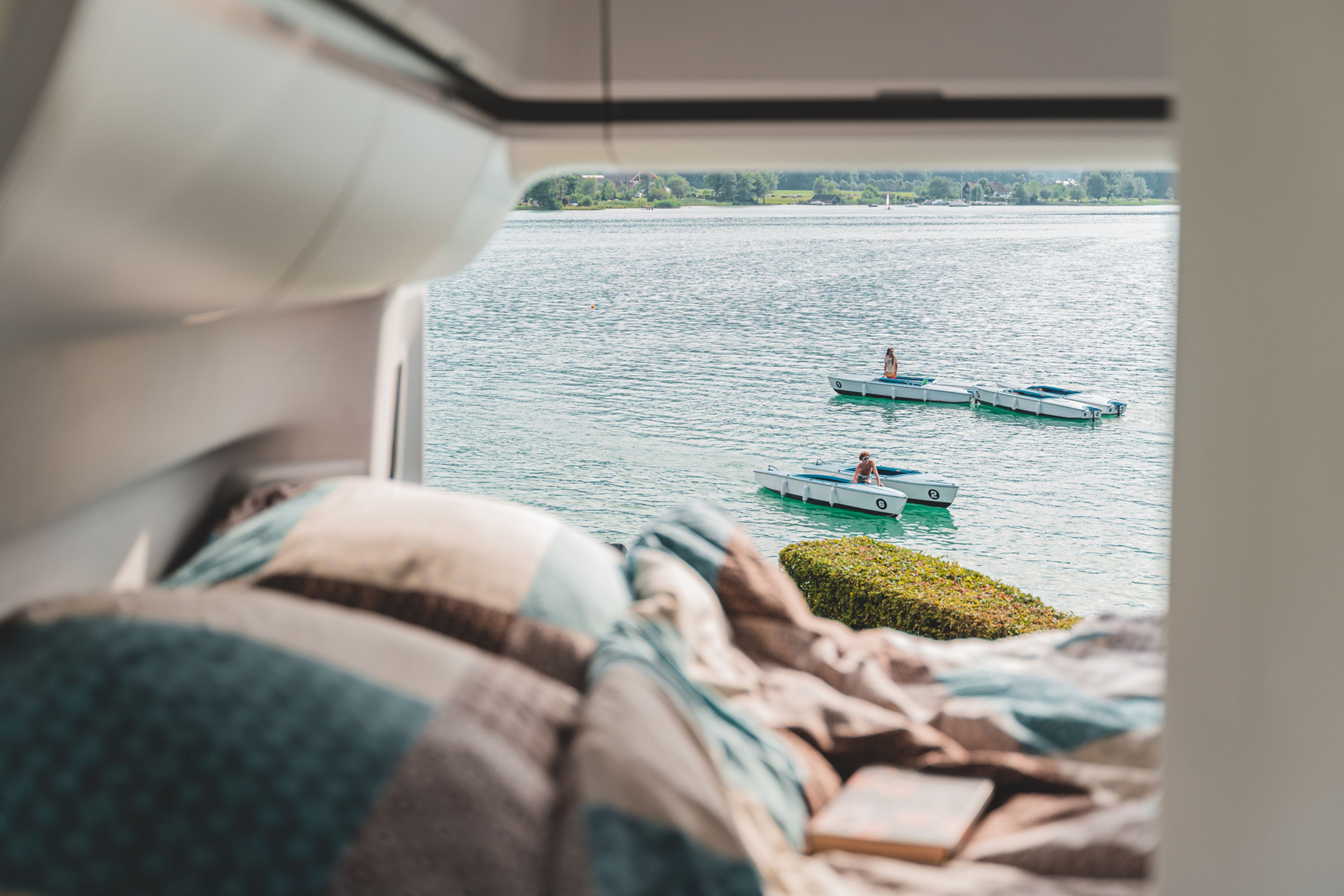 vista dall'interno del camper VW Grand California: si vedono persone che fanno canoa e kayak sul Lago Maggiore