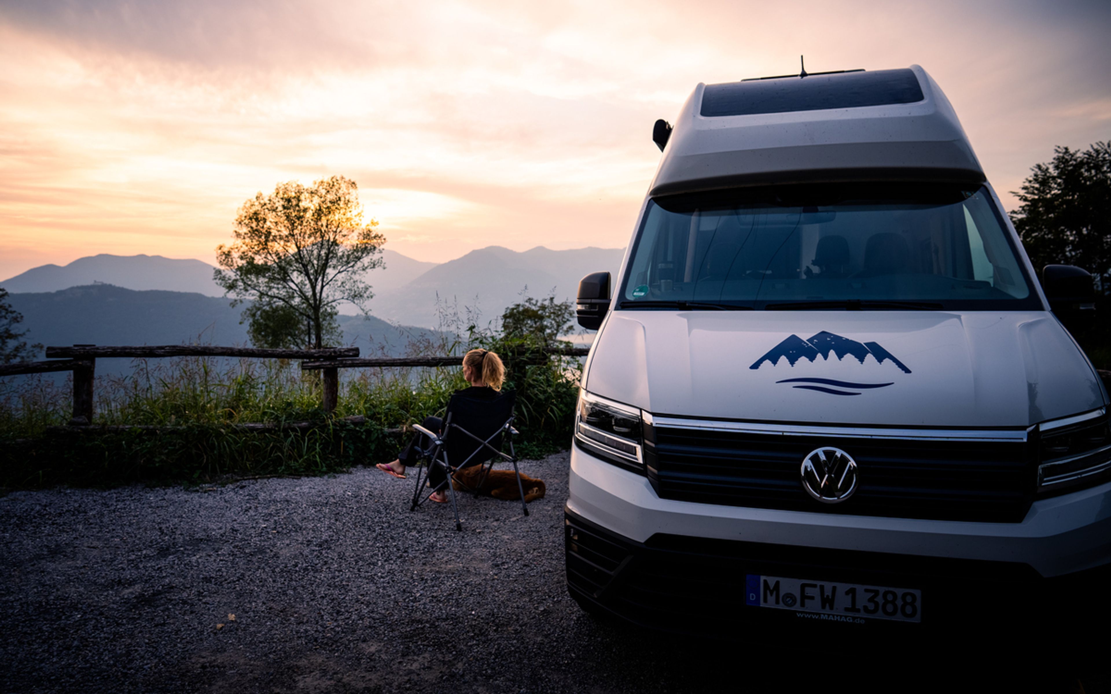A woman and her dog enjoying the sunset view of the Dolomites next to a camper van, the VW Grand California 600
